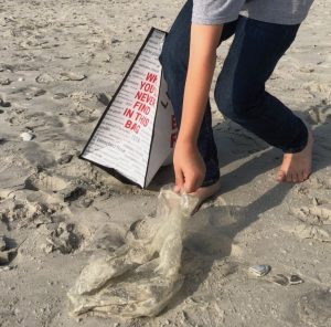 A student reaching down to pick up plastic from the shore. 