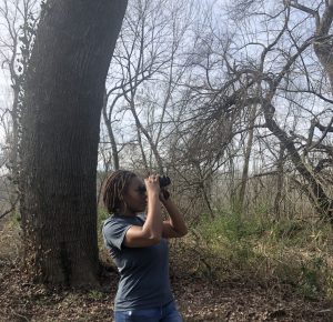 2018-19 Global Change Fellow and Graduate Student Intern, Deja Perkins peers through her binoculars toward a bird in the distance. 