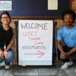 Interns Eleana and Zavier next to a registration sign for Tribal Climate Camp